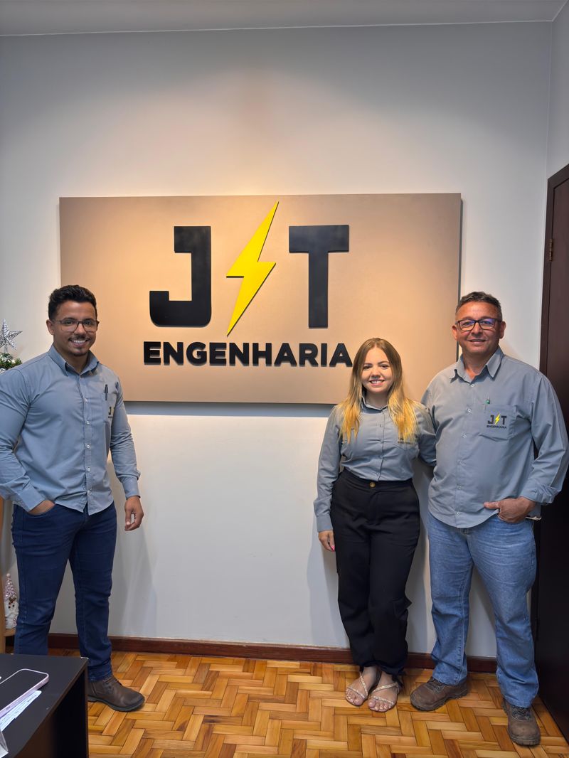 Sócios e equipe da JT Engenharia Elétrica em frente ao logo da empresa